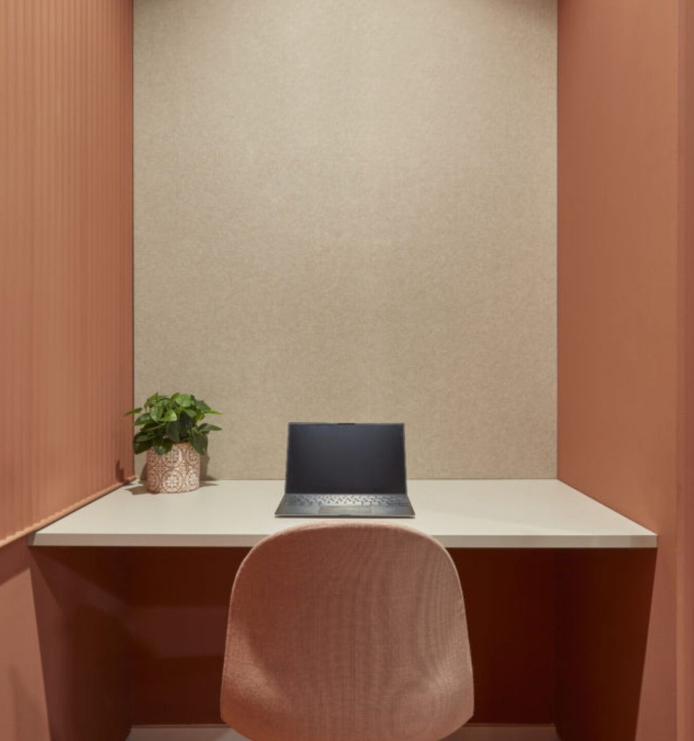 Cozy, minimalist office nook with peach walls, a small white desk, laptop, plant, and peach chair, evoking a calm and focused atmosphere