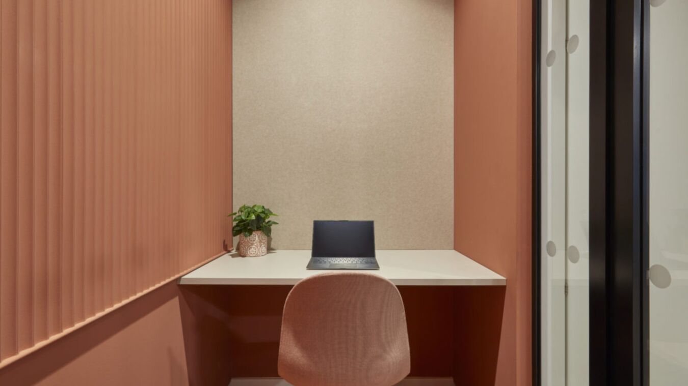 Cozy, minimalist office nook with peach walls, a small white desk, laptop, plant, and peach chair, evoking a calm and focused atmosphere