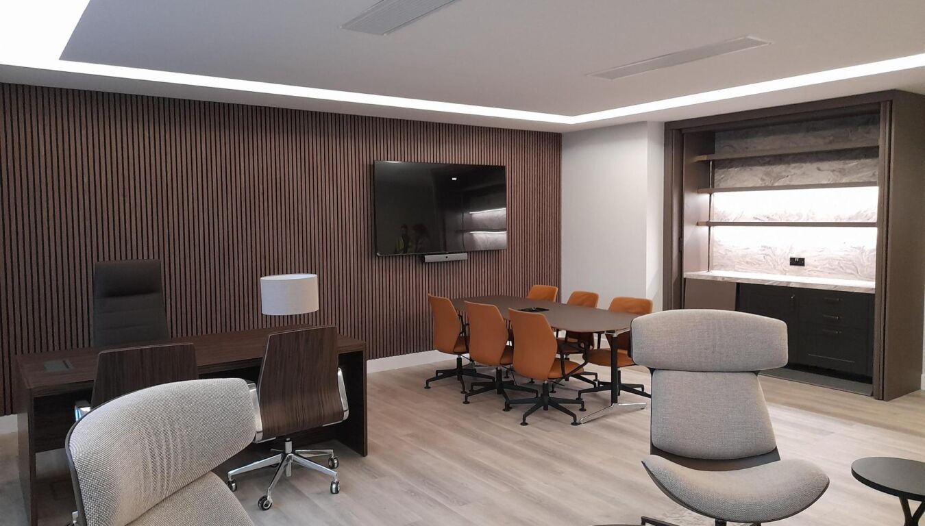 Modern office with a sleek design, featuring a large wooden desk, five orange chairs around a dark table, and a wall-mounted TV. Neutral tones create a calm, professional atmosphere