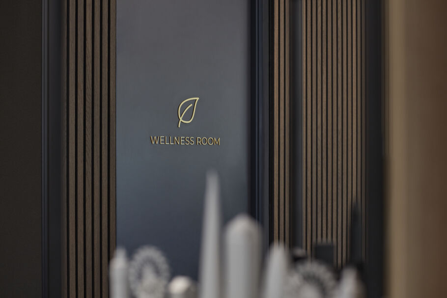A door labeled "WELLNESS ROOM" with a leaf symbol is set in a wood-paneled wall, creating a serene and inviting atmosphere.