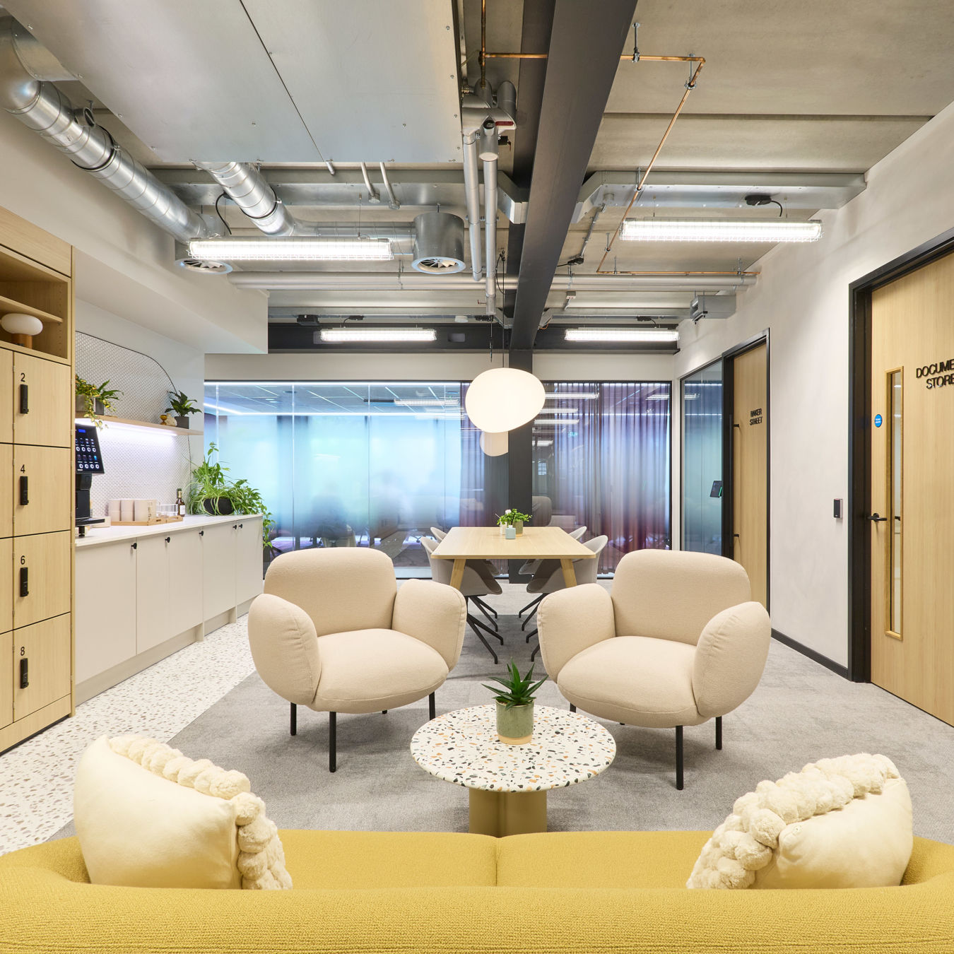 Modern office lounge with beige armchairs, yellow sofa, and a terrazzo coffee table holding a plant. Bright lighting, wooden cabinets, and a "Document Store" door.