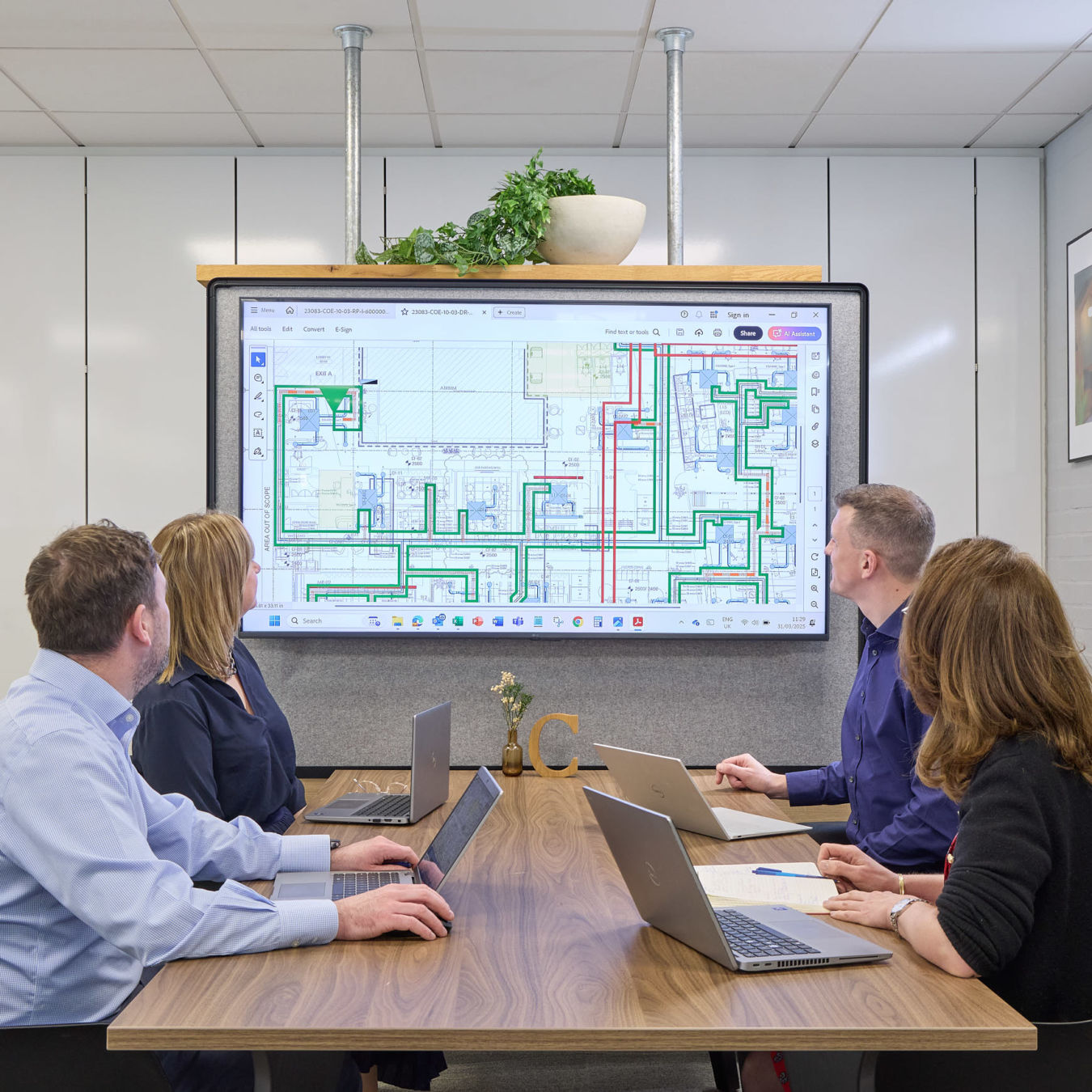 A team of four people sitting at a meeting table looking at a screen showing a building floor plan