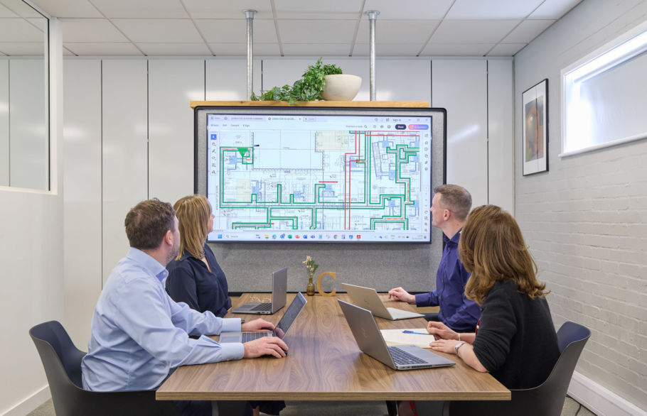 A team of four people sitting at a meeting table looking at a screen showing a building floor plan
